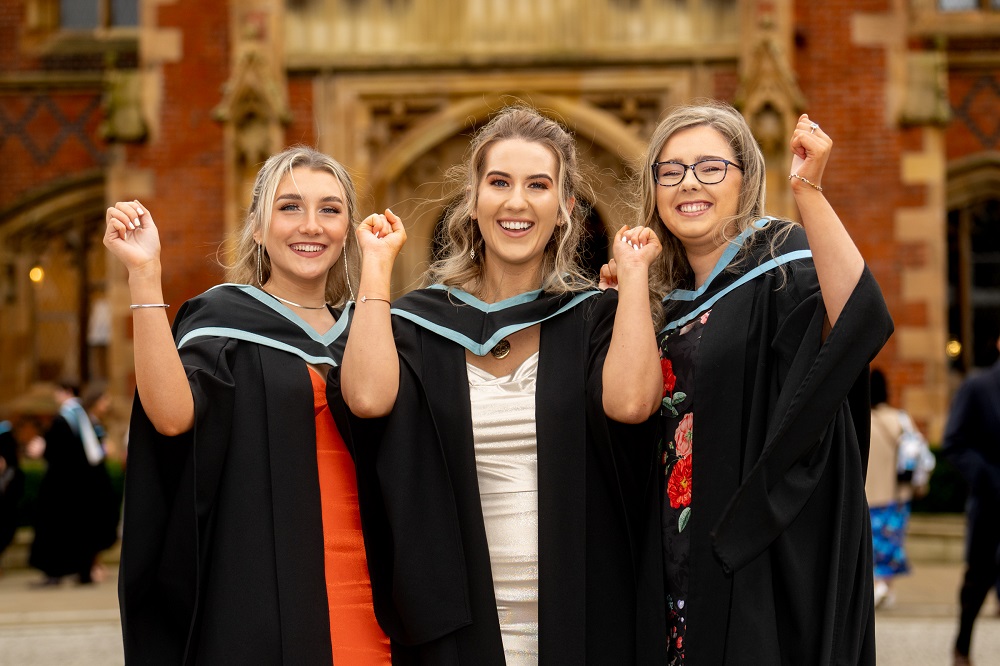 three new female graduates celebrating outside the Lanyon Building at Winter graduation 2023